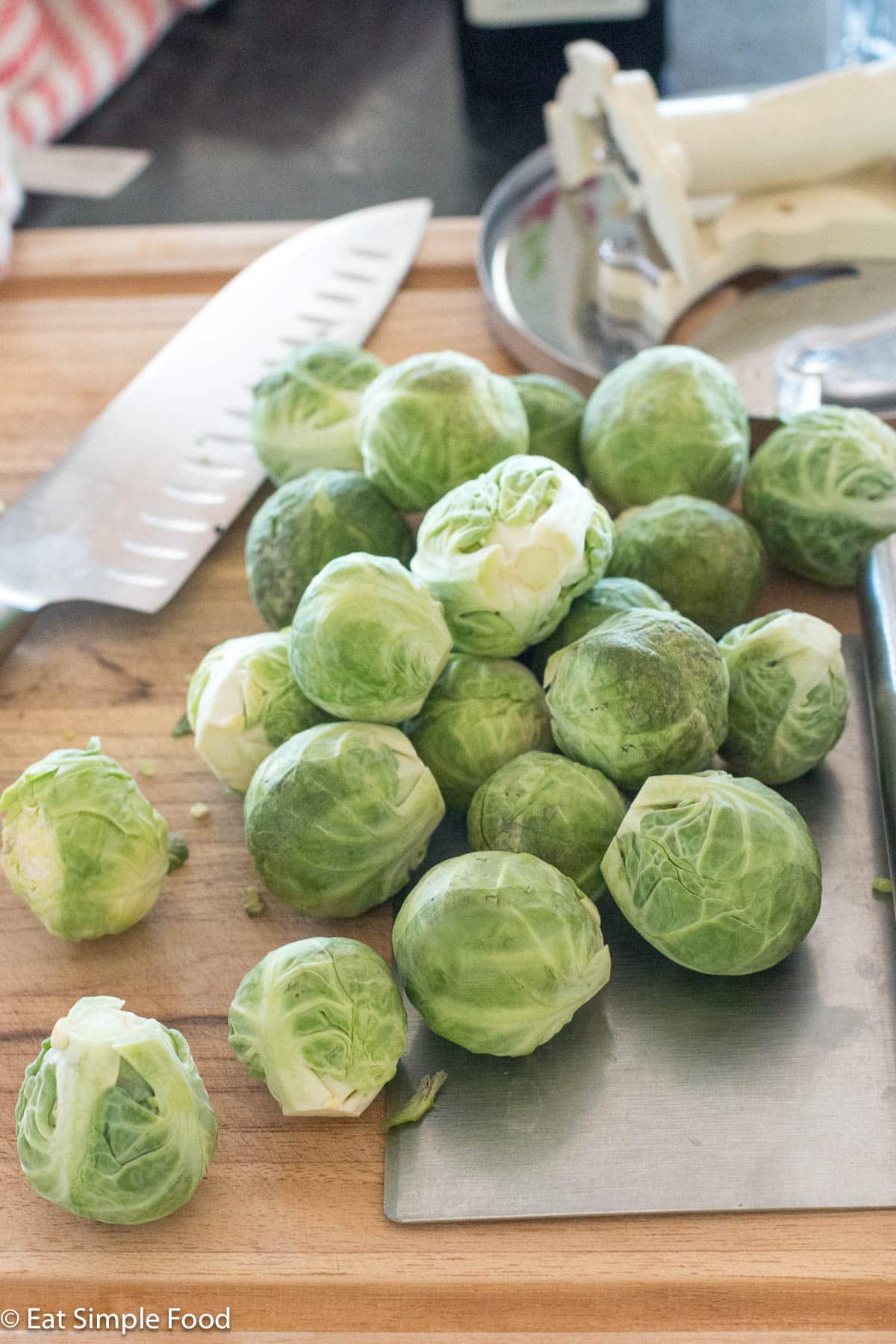 Whole Brussels sprouts on a wood cutting board with a chef's knife and a stainless steel pastry cutter.