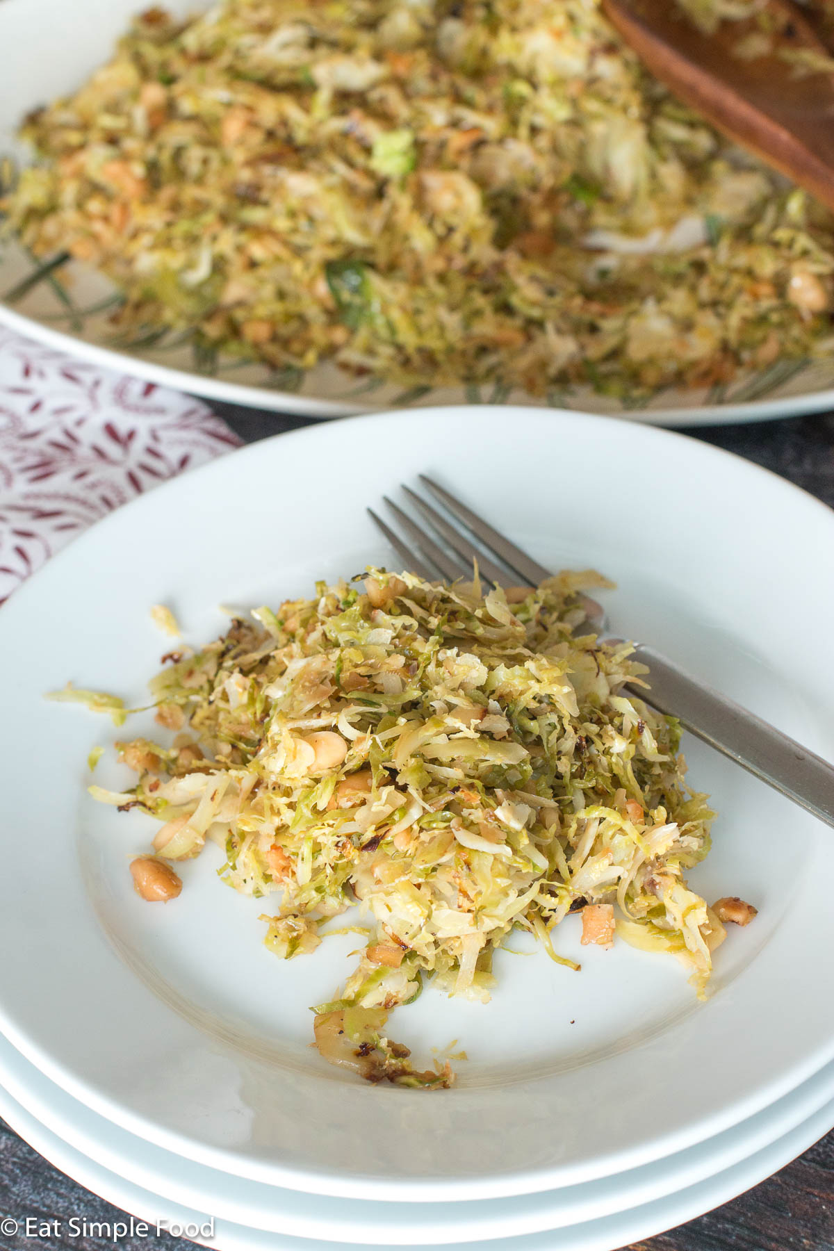 White plate with fork with sliced brussels sprouts and almonds. Larger plate in background.