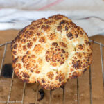 Browned whole head of cauliflower on an elevated rack above parchment paper. Side view.