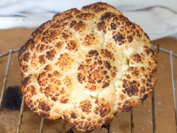 Browned whole head of cauliflower on an elevated rack above parchment paper. Side view.