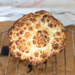 Browned whole head of cauliflower on an elevated rack above parchment paper. Side view.