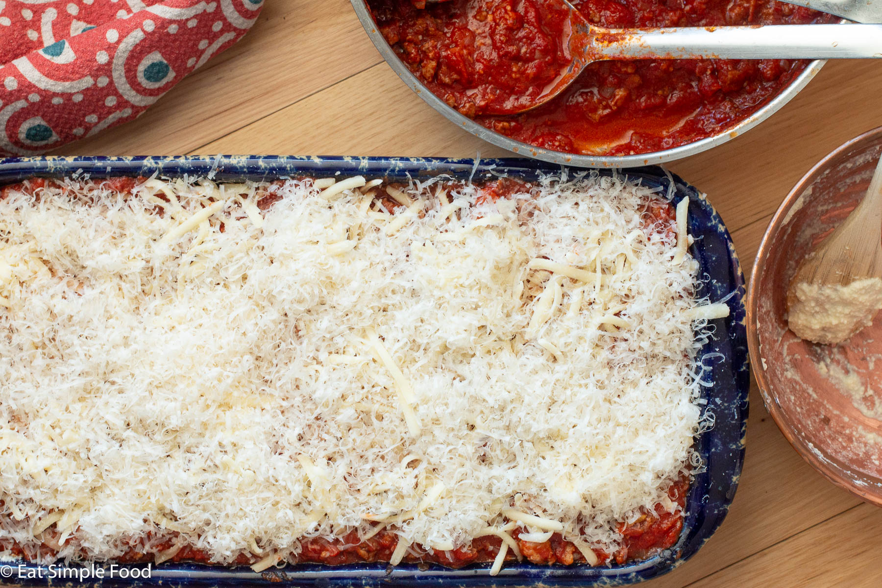 Top down view of a baking dish full of uncooked lasagna with grated white Parmesan and Mozzarella cheese on the top.