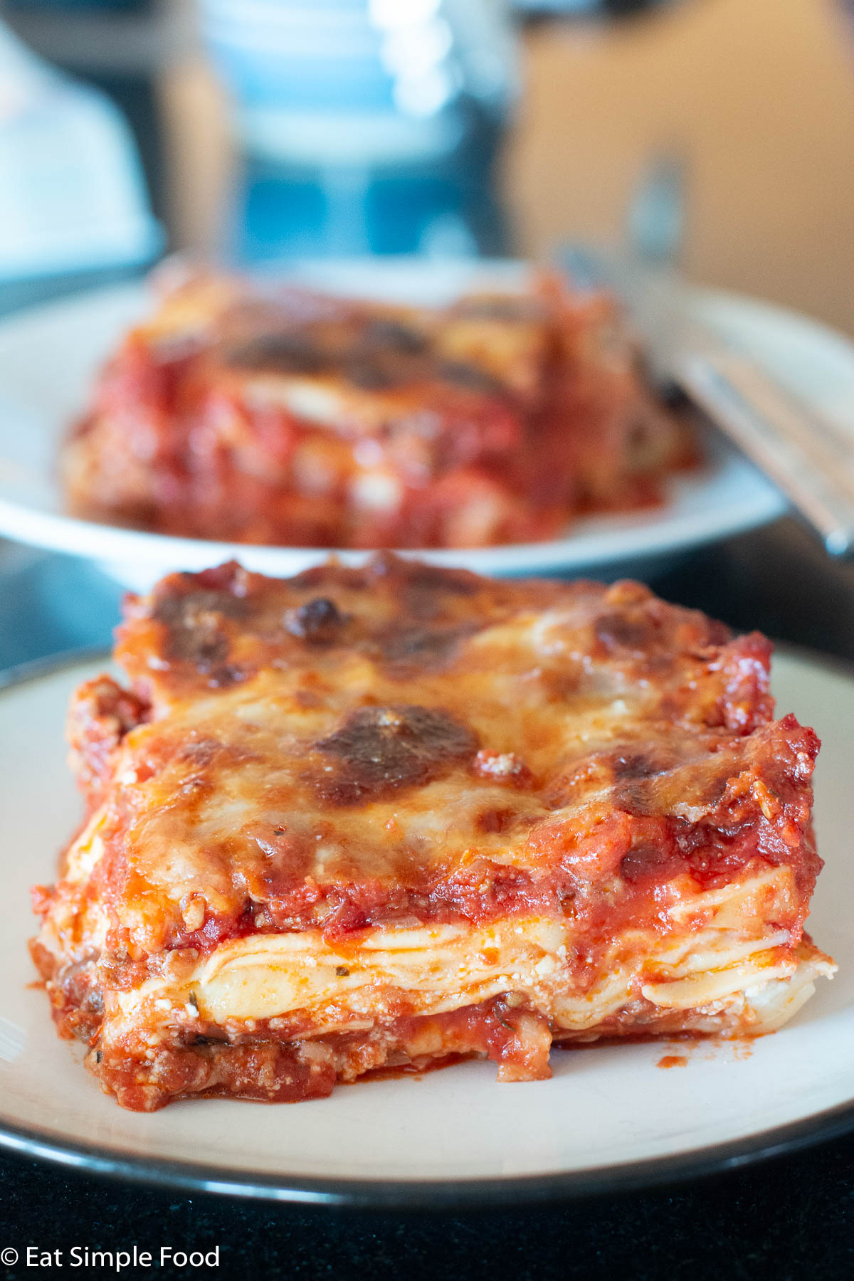 Slice of meat lasagna on a white plate with another slice in the background.