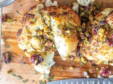 Roasted cauliflower half face down sprinkled with cranberries, pistachios, and chopped rosemary.