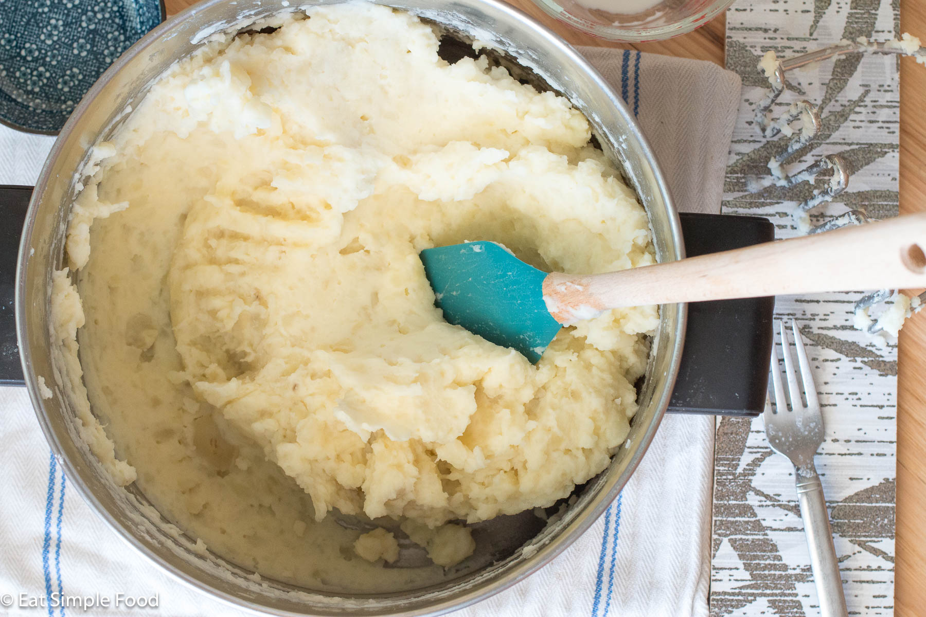 Top down view of a pot filled with mashed potatoes and a blue spatula with a wood handle hanging out.