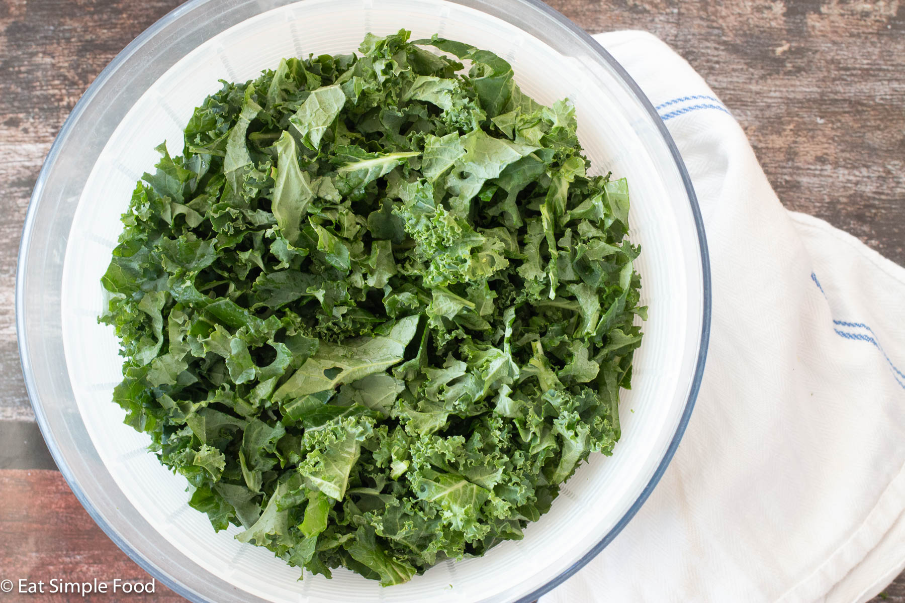Top down view of curly chopped green kale in a salad spinner with a napkin on the side.