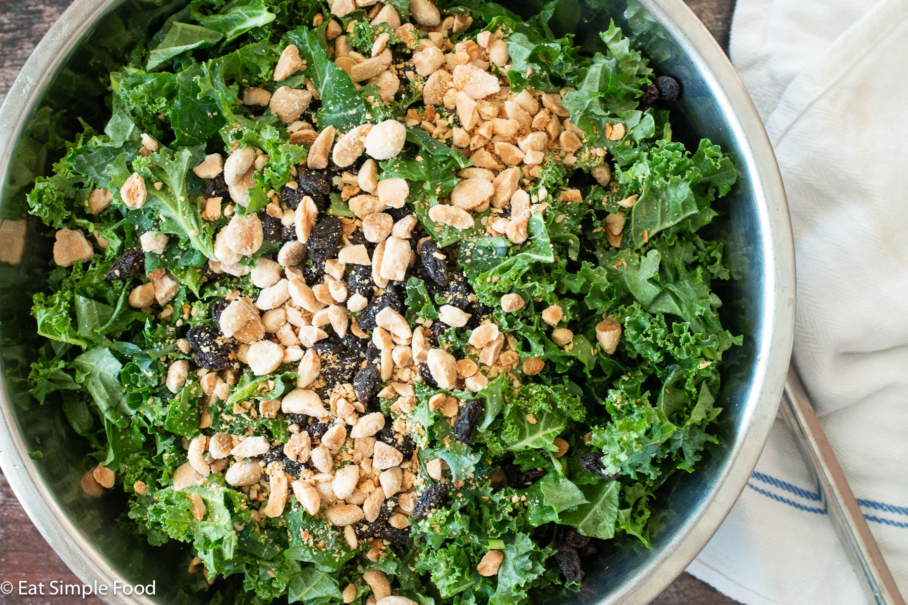 Top down view of a stainless steel bowl filled with chunky green kale, smashed almonds, and raisins.