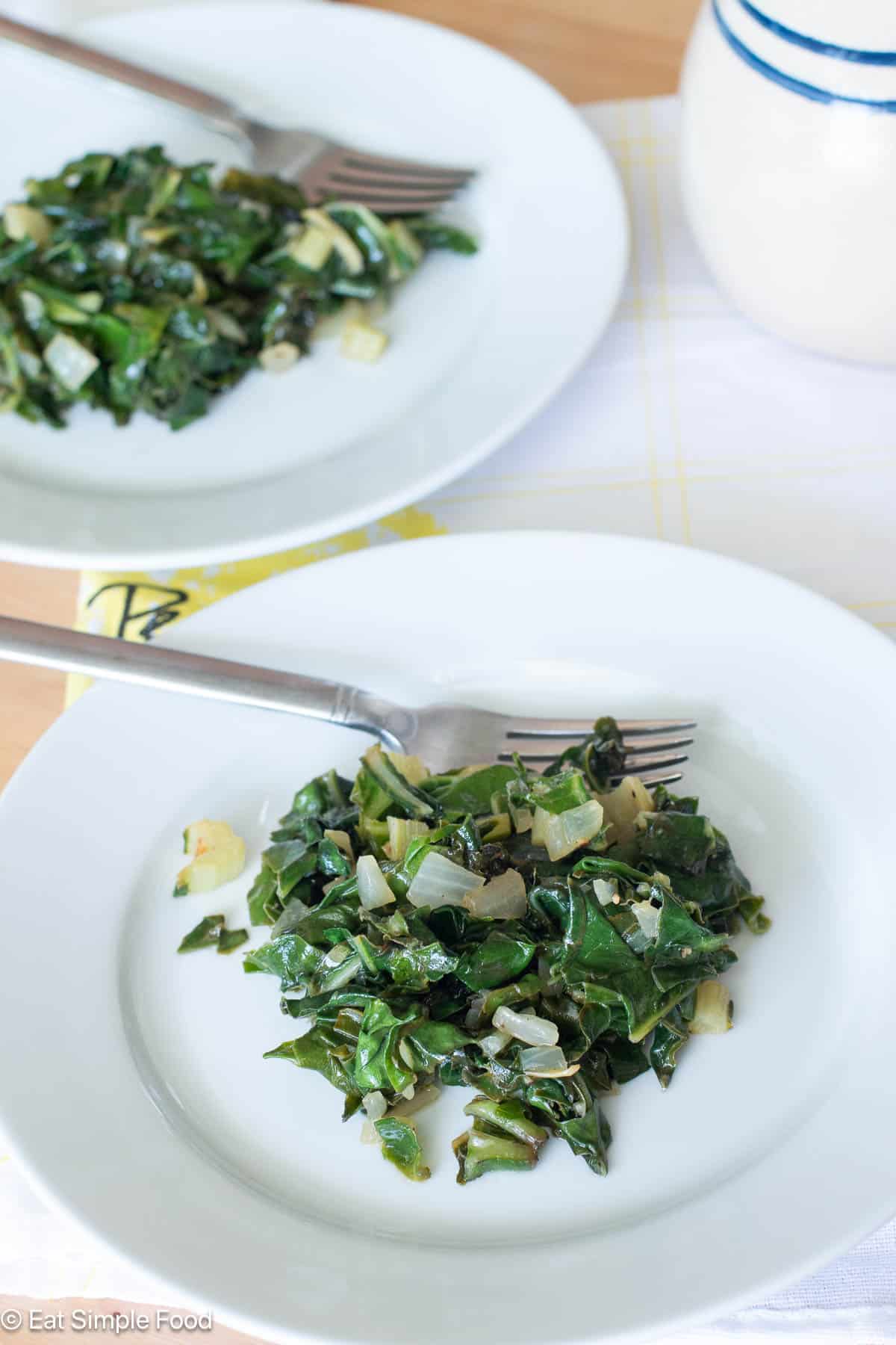 Two white plates with chopped cooked greens and onions. Both plates have a fork.