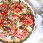 Round pie pan filled with sliced zucchini tomatoes with walnuts and cheese baked and crisp. 2 fork in the background. Close up.