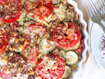 Round pie pan filled with sliced zucchini tomatoes with walnuts and cheese baked and crisp. 2 fork in the background. Close up.
