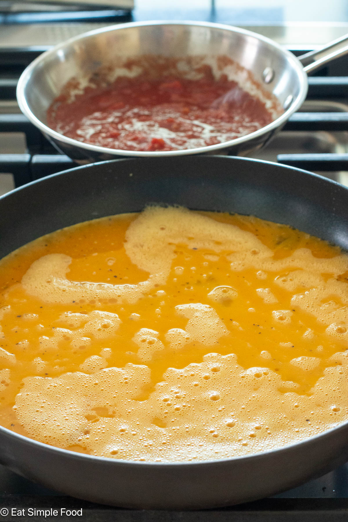 Pan of scrambled eggs cooking on a gas range with a pan of salsa cooking behind it.