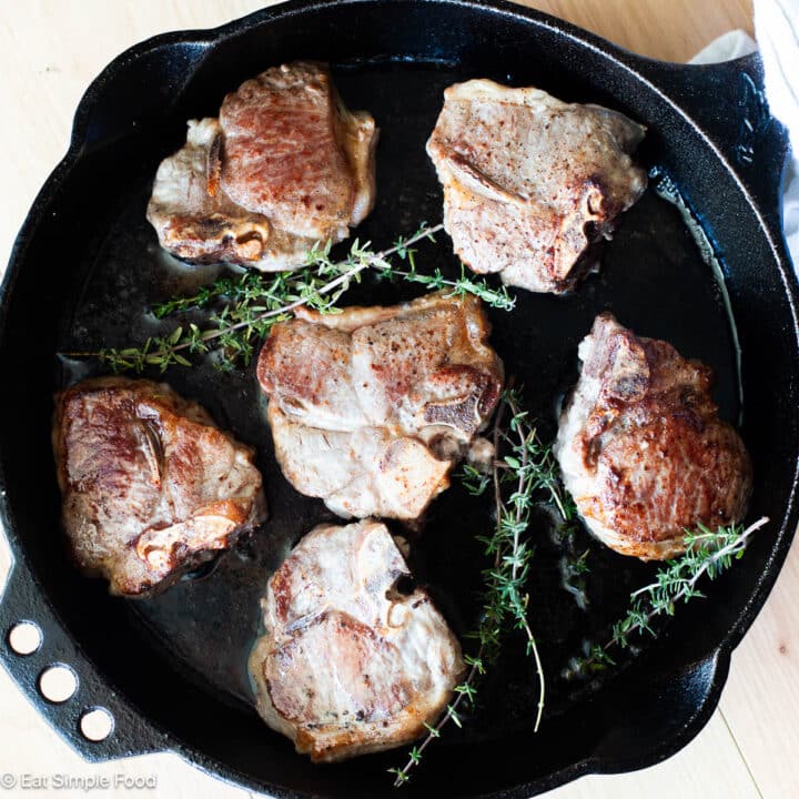 Top down view of 6 browned lamb loin chops with thyme sprigs in a cast iron skillet.