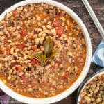 Top down view of a large white bowl of bean soup in broth with bay leaves on top. Close up.