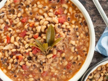 Top down view of a large white bowl of bean soup in broth with bay leaves on top. Close up.