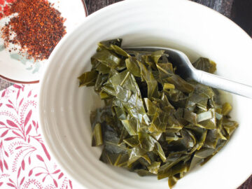 Top down view of white bowl with chopped greens and sauce in it. Small bowl of chili flakes on the side.