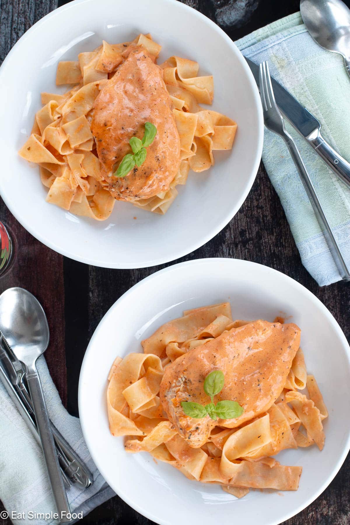 Top down view of two white plates with noodles and an orange sauce with napkins and utensils.