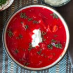 Top down view of a bowl of red soup with sour cream and chopped dill on top.