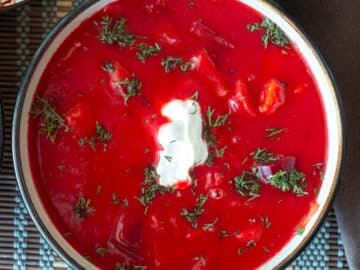 Top down view of a bowl of red soup with sour cream and chopped dill on top.