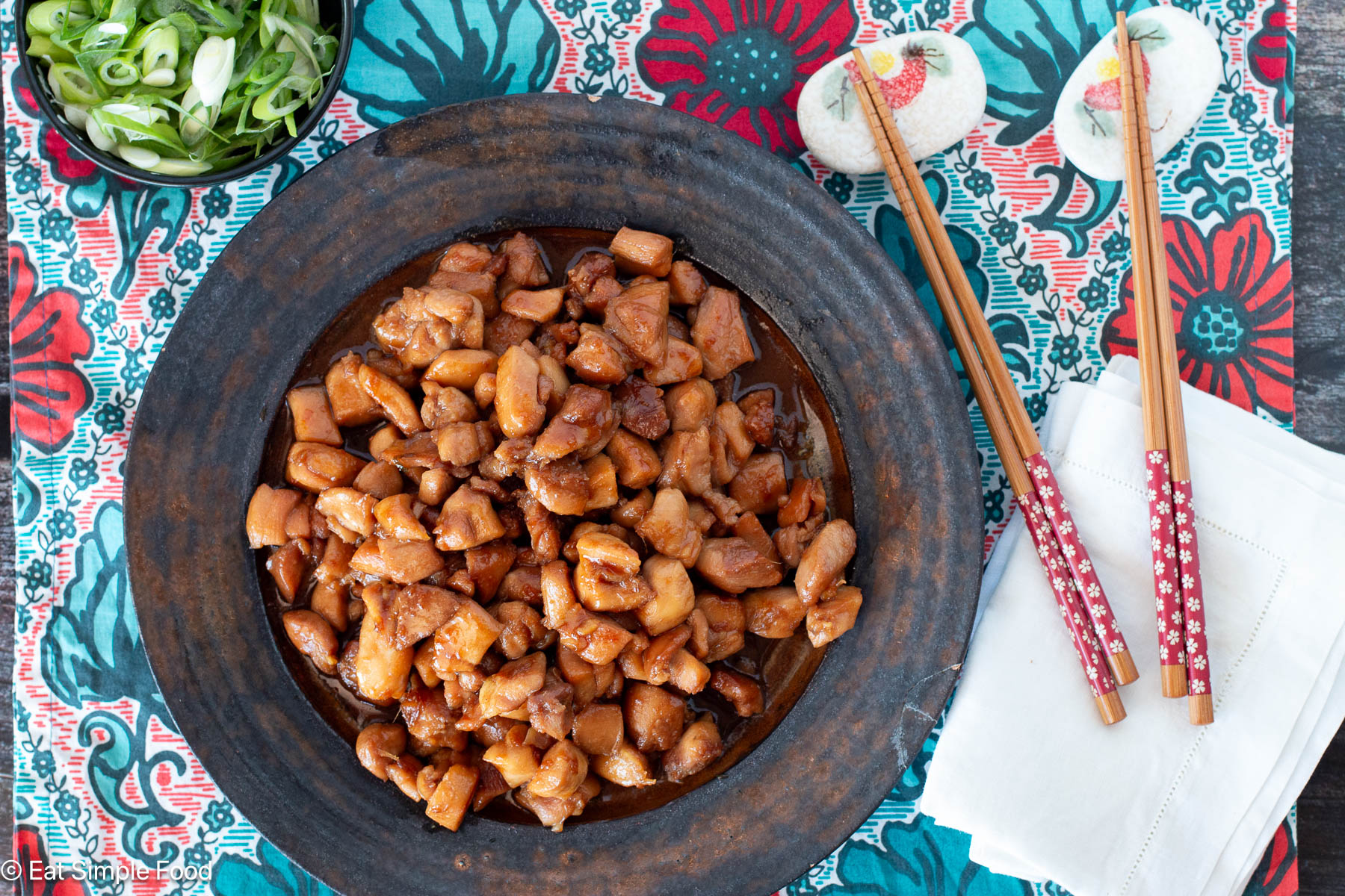 Top view of brown plate with diced chicken in brown sauce. chopsticks and white napkins on the side.