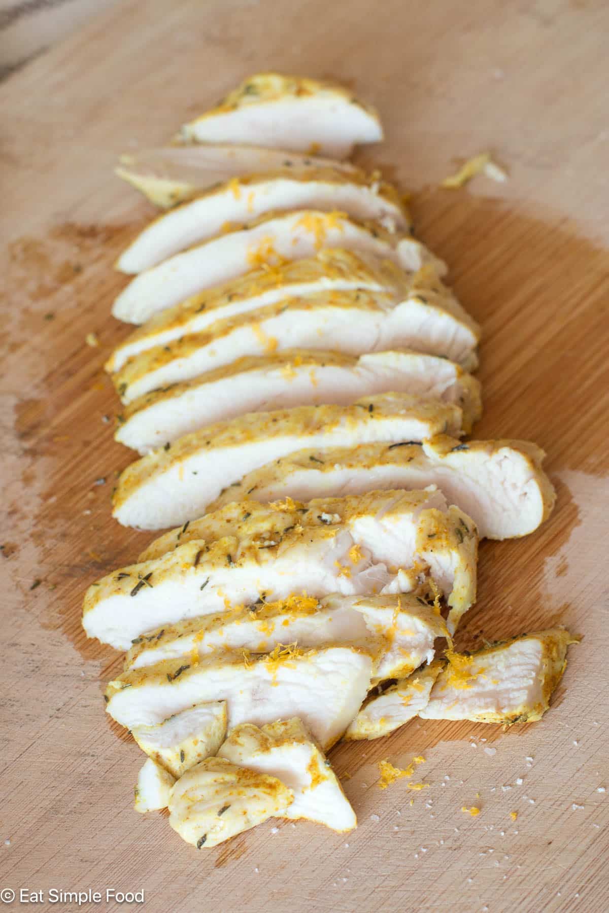 Sliced chicken breast with juices on a wood cutting board.