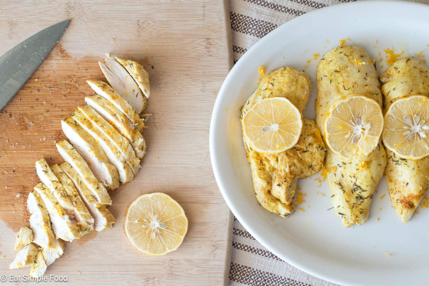 top down view of 3 chicken breast with lemon on top on a white plate and sliced chicken with a lemon slice on a wood cutting board.