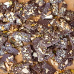 Close up and top down view of broken pieces of dark chocolate with nuts on top.