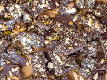Close up and top down view of broken pieces of dark chocolate with nuts on top.