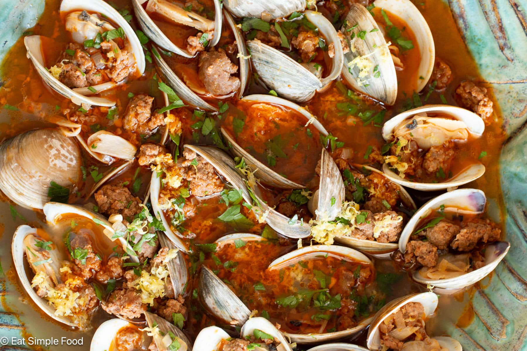 Close up of top down view of open cooked clams with ground sausage in a green bowl.