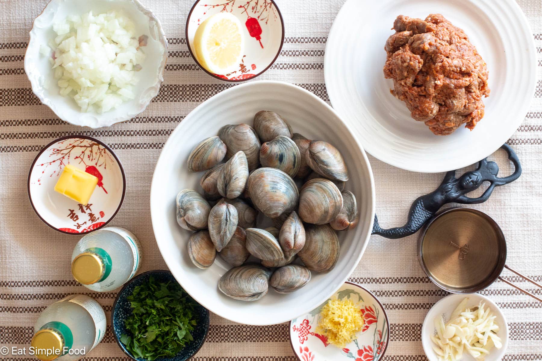 top down view of bowl of clams with separate containers of butter, lemon zest, garlic, diced onions and sausage.