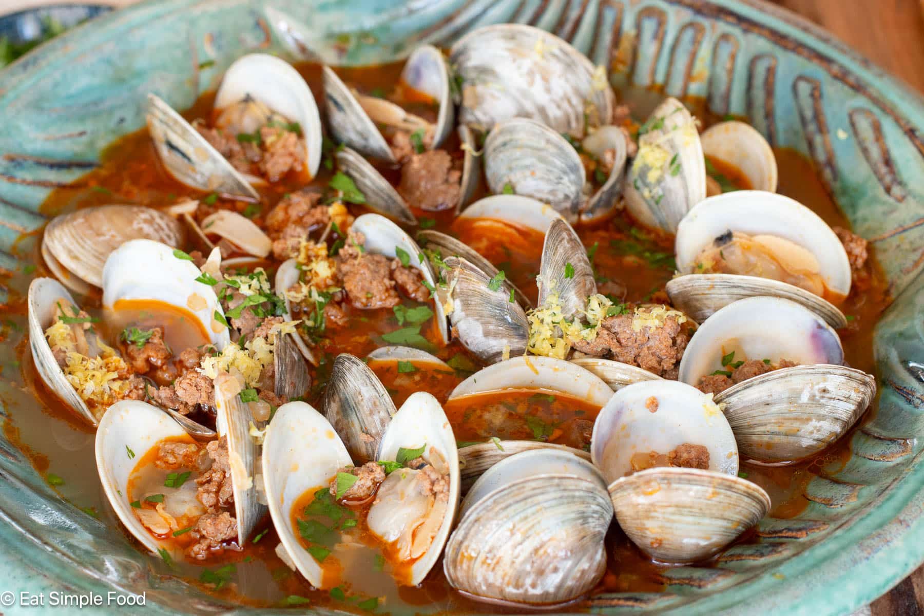 Side view of open clams and sausage in red sauce in a green bowl.