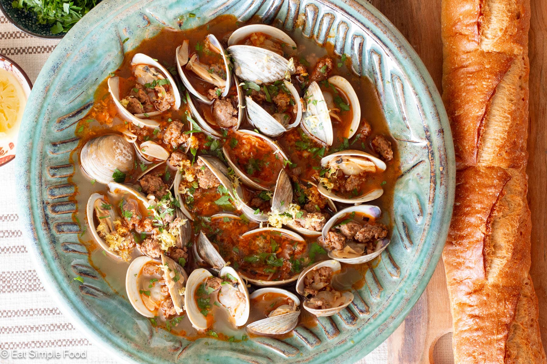 Top down view of clams and sausage in a green bowl with a baguette on the side.