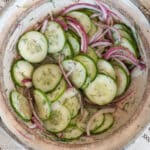 Top down view of sliced cucumbers and red onions in a tan bowl. Close up.
