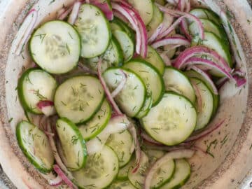 Top down view of sliced cucumbers and red onions in a tan bowl. Close up.