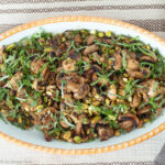 Top down view of white oval bowl filled with cooked mushrooms with pistachios and chopped basil. Close up.