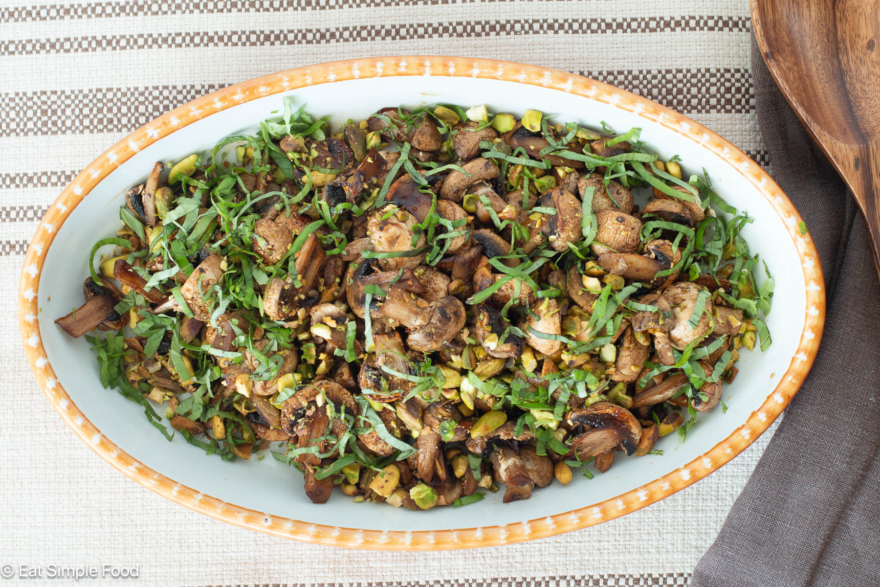 Top down view of white oval bowl filled with cooked mushrooms with pistachios and chopped basil.