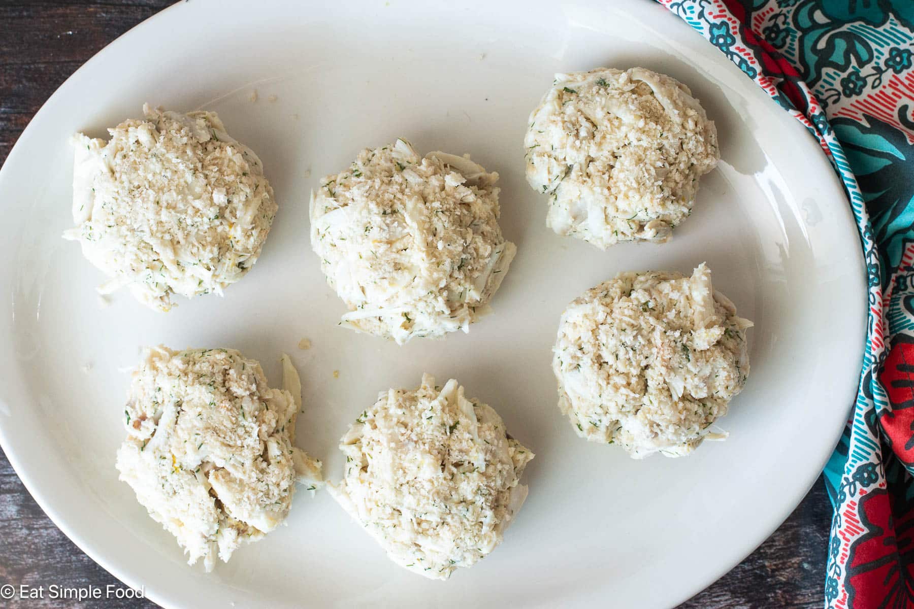Top down view of raw crab cakes on a white plate.