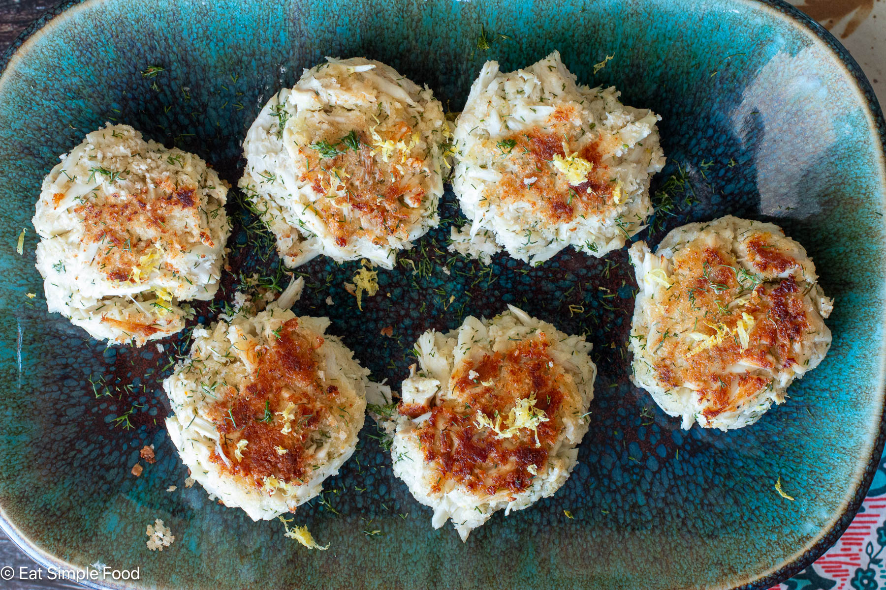 Top down view of seared crab cakes on an aqua rectangle plate.