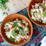 Top down view of a wood bowl of pasta salad with basil and silverware on the side.