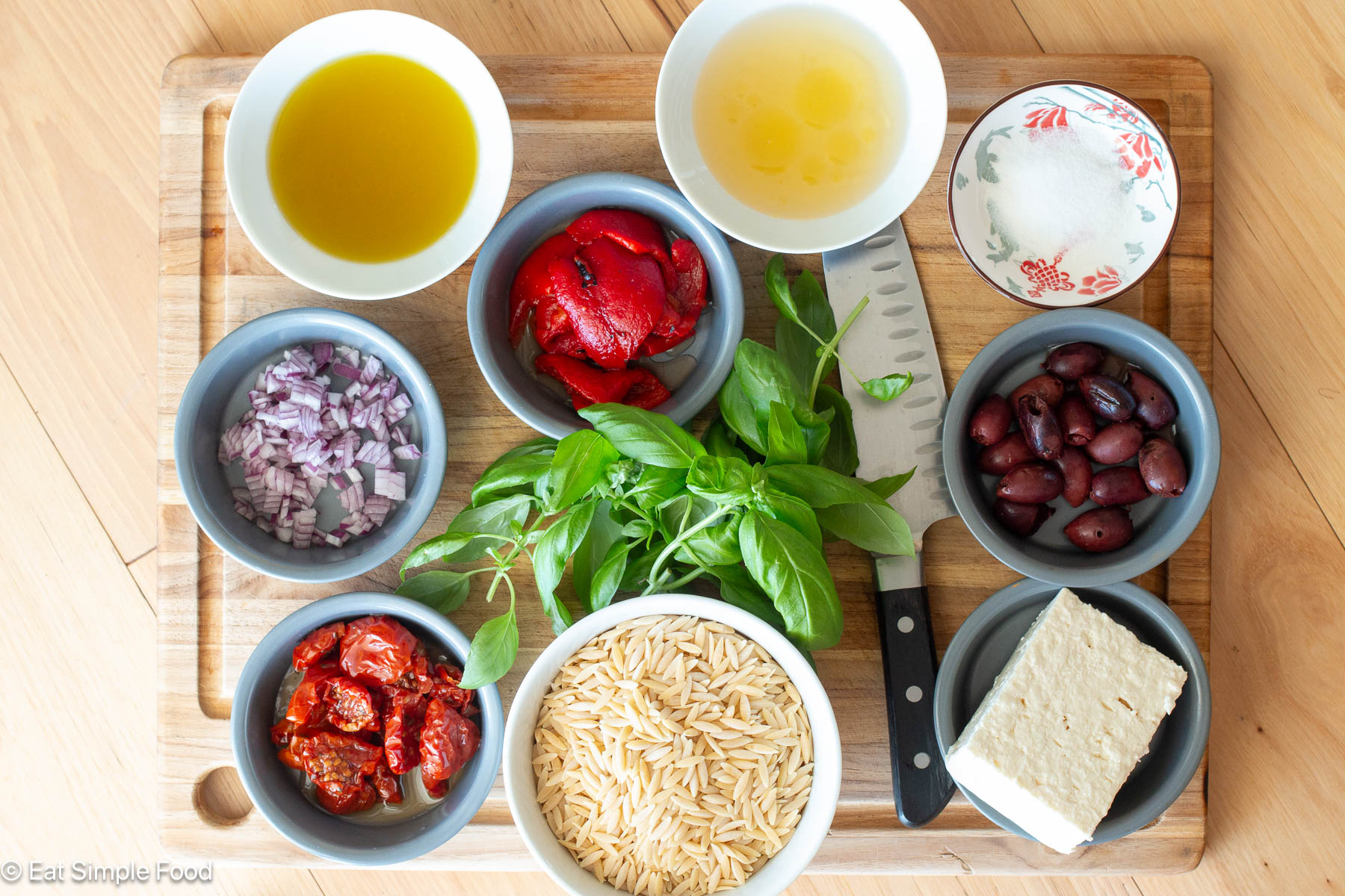Top down view of bowls of ingredients on a wood cutting board with a chefs knife.