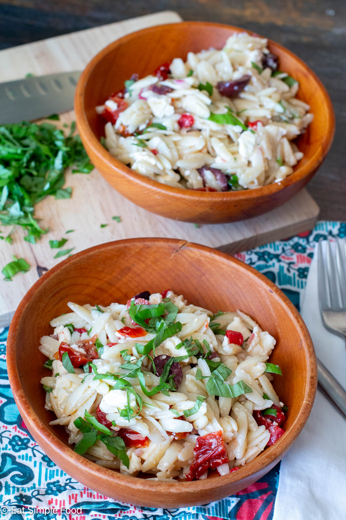 Side view of two wood bowl filled with pasta on a colorful tablecloth.