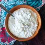 Top view of wood bowl filled with white mayonnaise sauce with pickles.