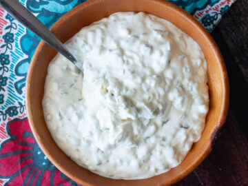 Top view of wood bowl filled with white mayonnaise sauce with pickles.