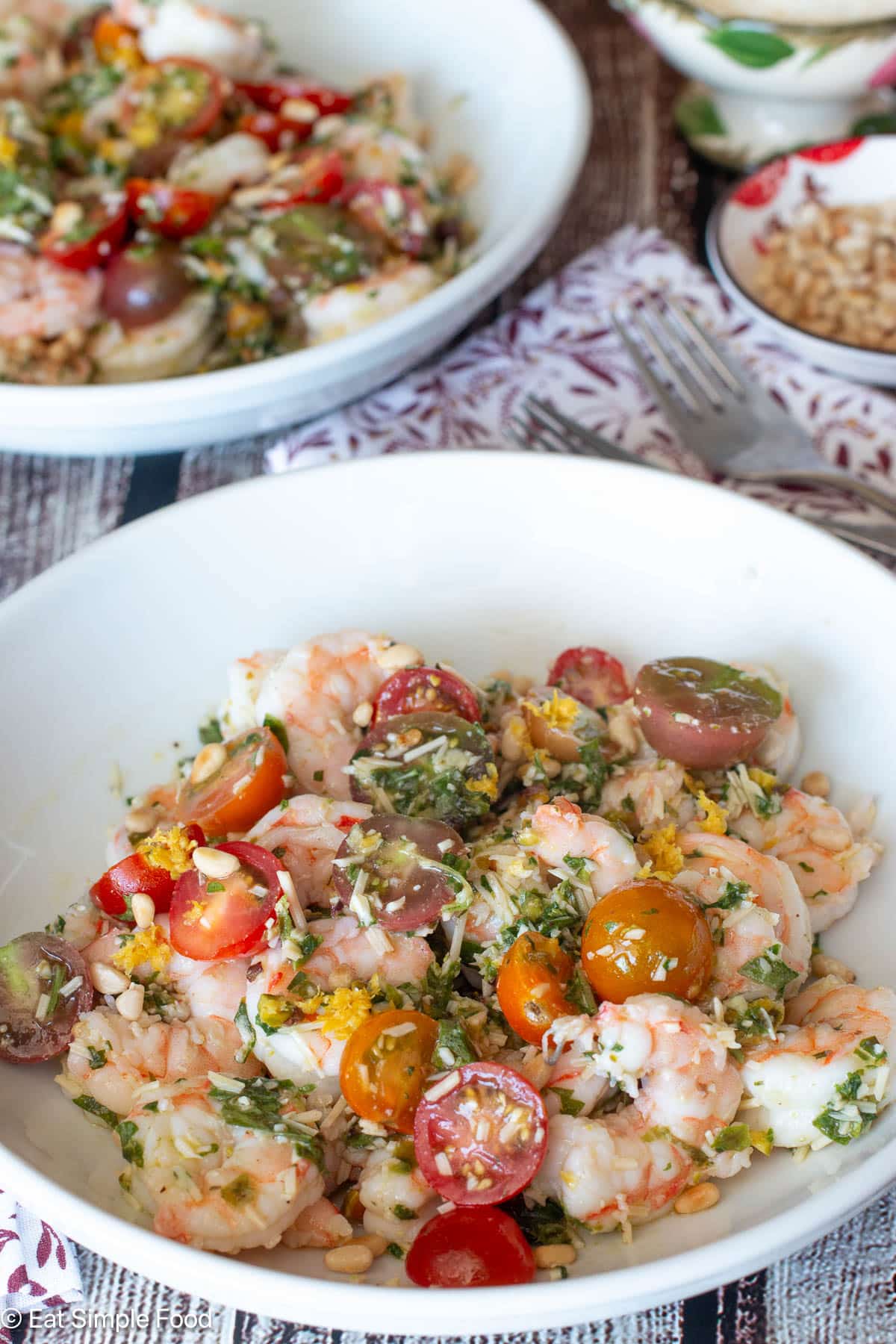 Two white plates filled with poached shrimp, basil pesto, and halved cherry tomatoes.