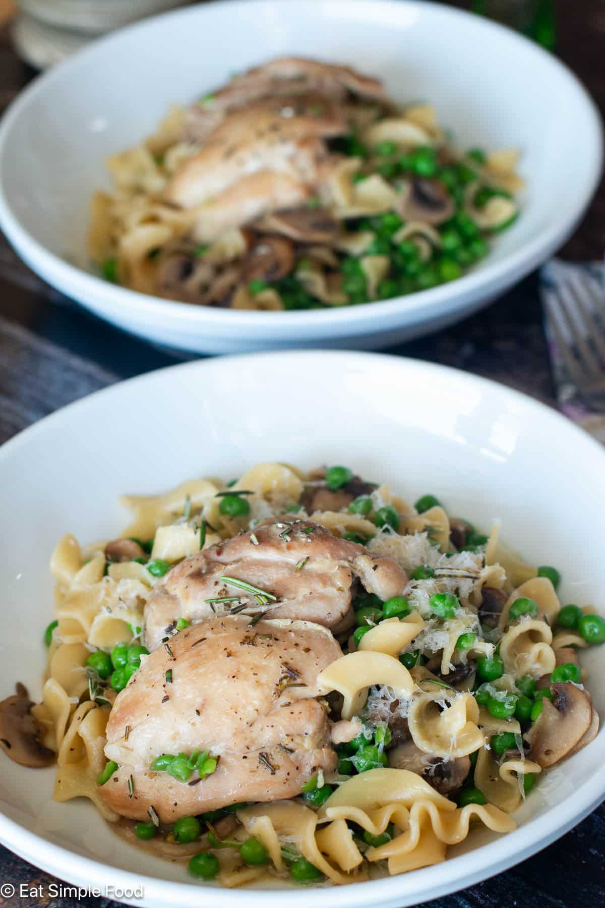 Two white plates with chicken thighs over egg noodles with mushrooms and peas.