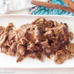 White plate with browned meat slices with colorful napkin in background.