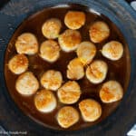 Top down view of cooked scallops on a brown plate in a brown orange sauce.