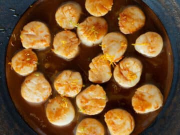 Top down view of cooked scallops on a brown plate in a brown orange sauce.