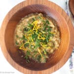 Wood bowl of brown dip garnished with chopped parsley and lemon zest. Purplee and white napkin in background. Top view. Close up.