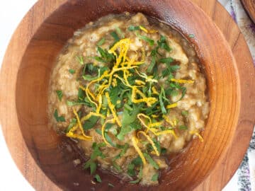 Wood bowl of brown dip garnished with chopped parsley and lemon zest. Purplee and white napkin in background. Top view. Close up.