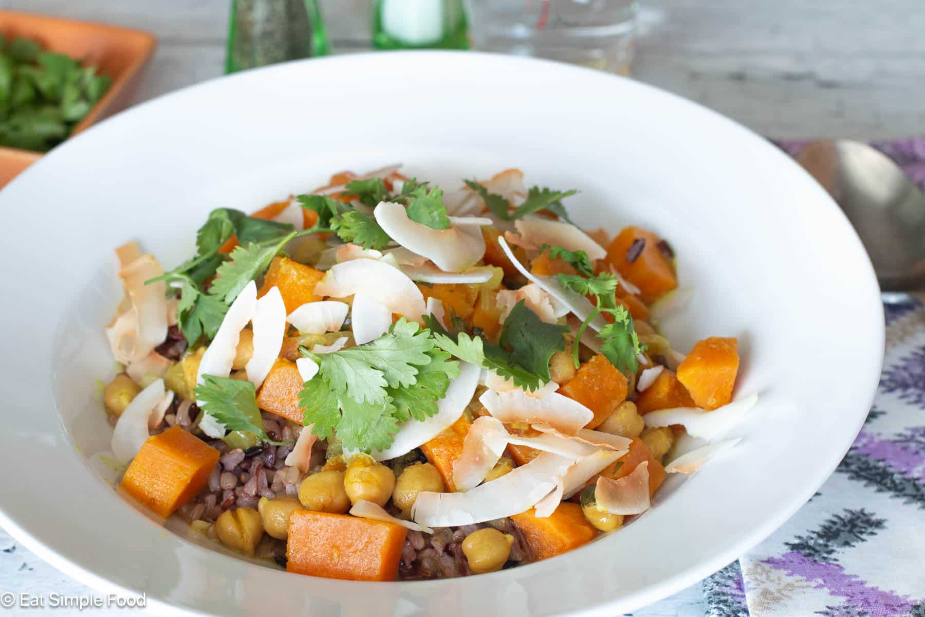 White Plate with cubed sweet potatoes and chickpeas over wild rice with cilantro and white coconut flakes.